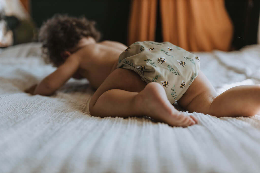 Baby laying on a bed in a Bayrli Deluxe all-in-one cloth diaper in Bumble Bee print